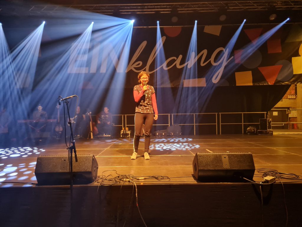 Dziewczyna z mikrofonem w dłoni stoi na scenie.