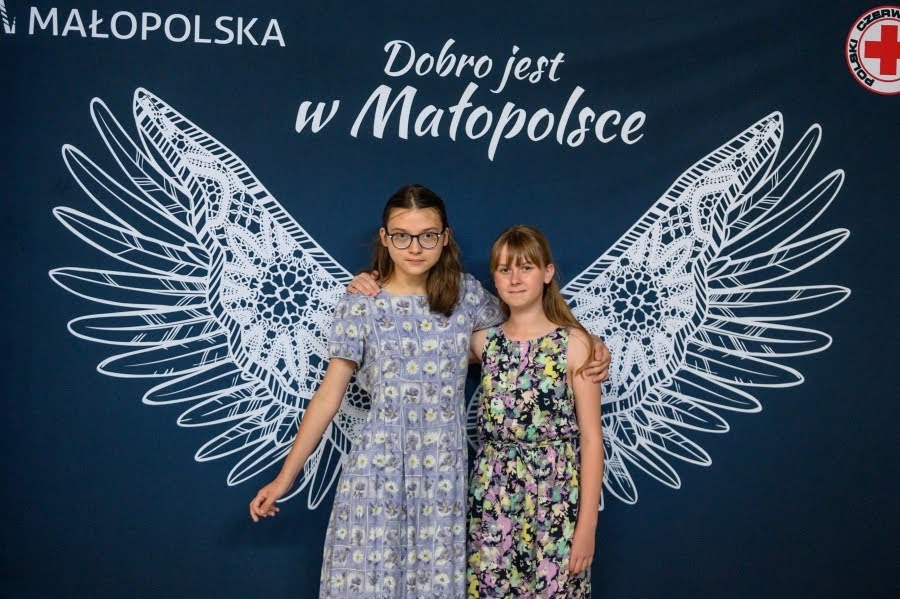 Dwie dziewczynki stoją na tle granatowego baneru promującego projekt Wizytówki Małopolski